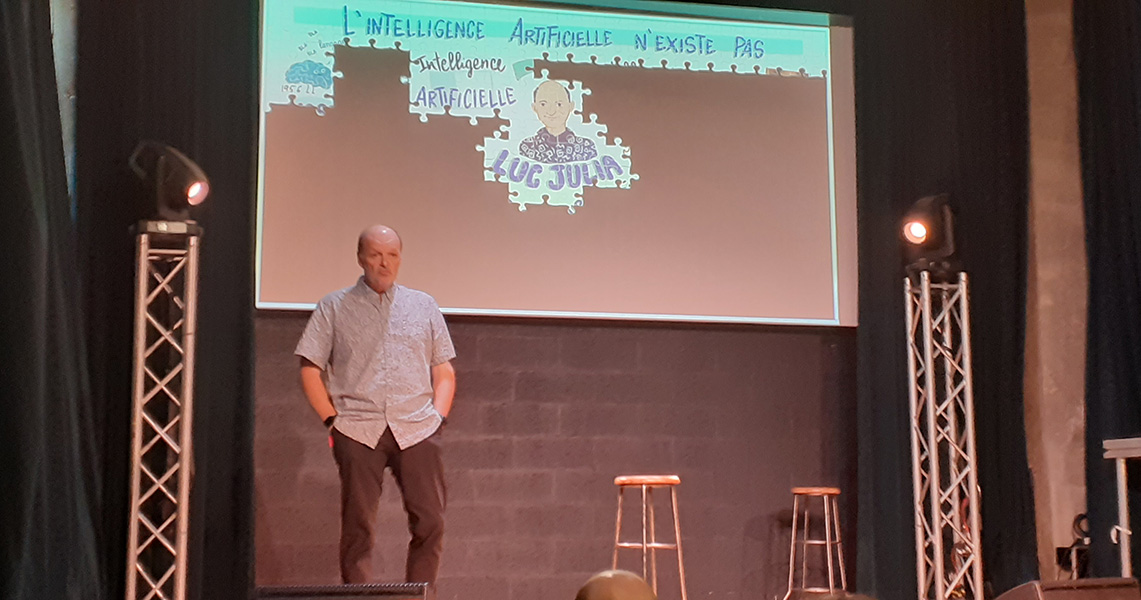 Luc Julia on stage with a presentation projected behind him