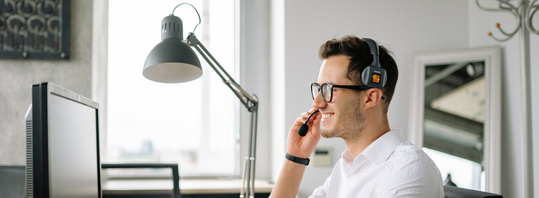 Homme souriant avec un casque microphone sur la tête face à un ordinateur